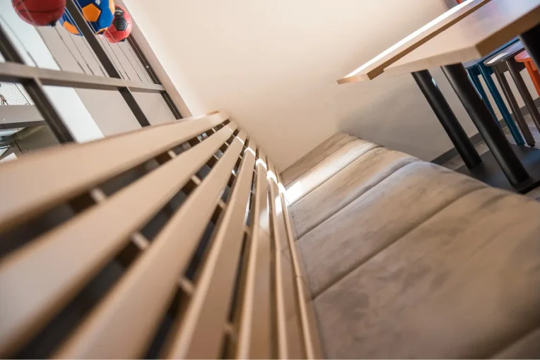 Foto, die die Inneneinrichtung des Speisaals der Sport Jugendherberge in Rheine, Holzstühle Mattis in bunt orange, blau und graubeige, Säulentische, helle HPL Tischplatten, Lattenbank mit Sitzpolster