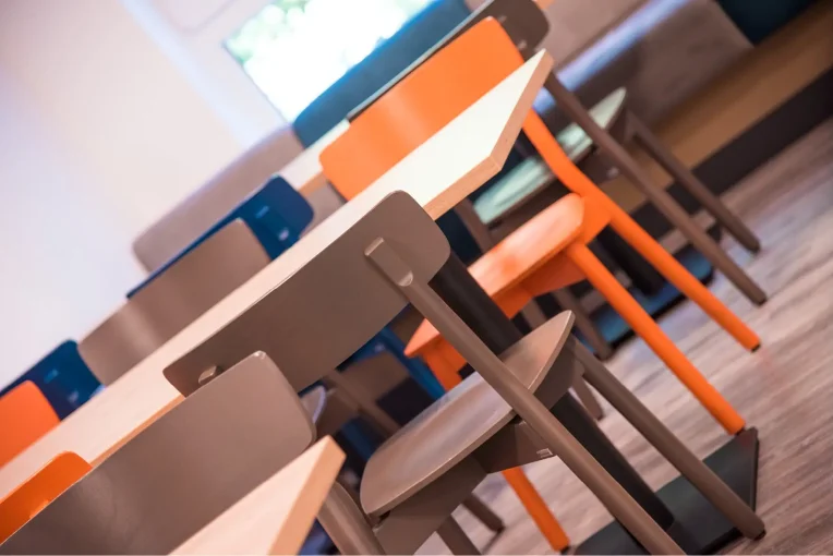 Foto, die die Inneneinrichtung des Speisaals der Sport Jugendherberge in Rheine, Holzstühle Mattis in bunt orange, blau und graubeige, Säulentische, helle HPL Tischplatten