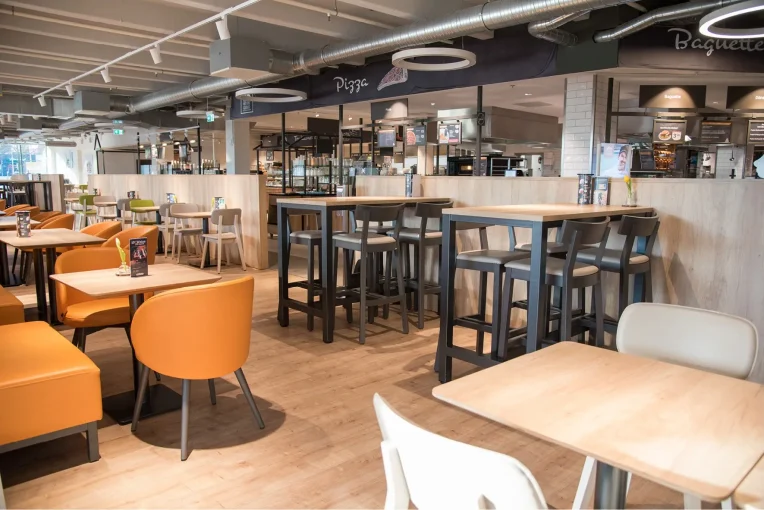 Möblierung, Sessel in orange, Stühle Joris, Gestell weiß, Polster grau und grün, Polsterbank in Orange, Säulentische, Tischplatte mit HPL belegt, Hocker Ole an Stehtischen, Gastronomie Globus Castrop Rauxel Schniedersitzt