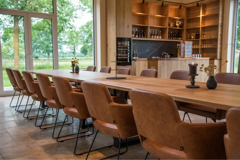 Foto Einrichtung Trüffelscheune Event-Location, lange Tafel, Tischplatte Eiche massiv Sessel Marvin Bezug Echtleder braun, Küche im Hintergrund