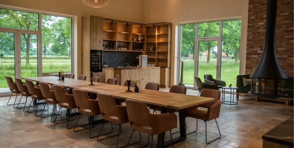 Foto Einrichtung Trüffelscheune Event-Location, lange Tafel, Tischplatte Eiche massiv Sessel Marvin Bezug Echtleder braun, Küche im Hintergrund